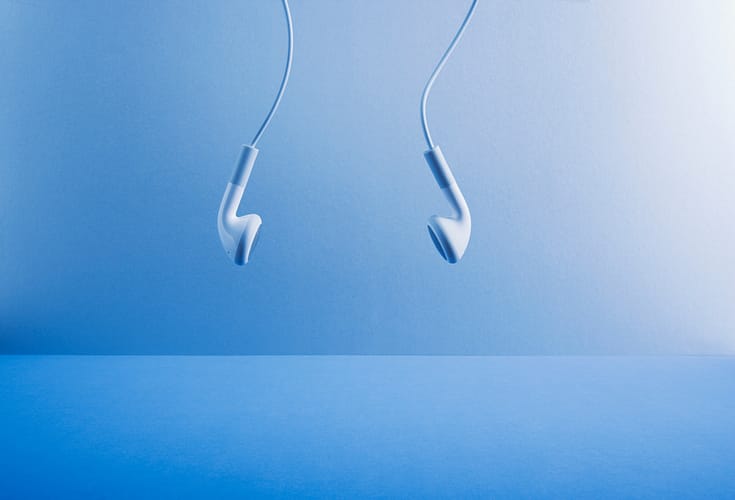 Image of white headphones hanging against a blue background.