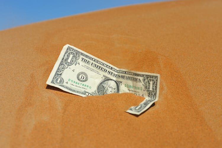the greenback is half buried into real desert sand concept image of financial trouble.