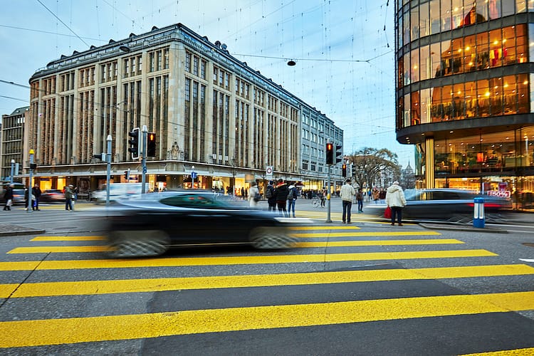 Busy Zurich street scene with blurred electric car and pedestrians. Luxury electric cars are popular in Zurich. In the background are retail shops and offices. Zürich often ranks in the top ten most liveable cities in the world.